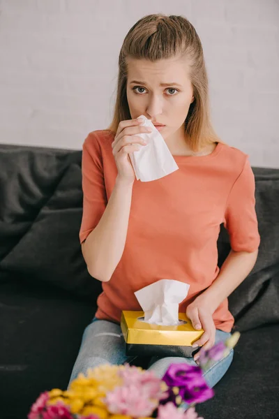 Foyer sélectif de fille triste attrayant avec du pollen allergie tenant tissu et regardant caméra près des fleurs — Photo de stock