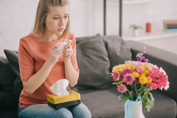 Schöne blonde Frau mit Pollenallergie hält Gewebe in der Hand und betrachtet Blumen in der Vase — Stockfoto