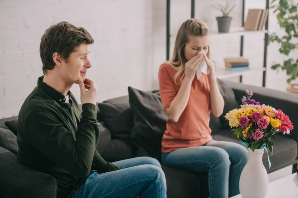 Nachdenklicher Mann blickt auf Vase mit Blumen neben niesendem blondem Mädchen mit Pollenallergie — Stockfoto