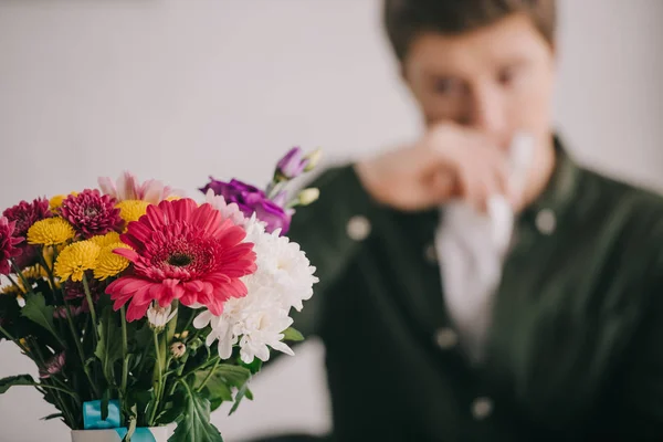 Selective focus of blooming flowers near sneezing man with pollen allergy — Stock Photo