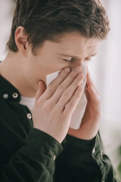 Закрыть глаза на человека, страдающего аллергией и чихающего в тканях с закрытыми глазами дома — стоковое фото