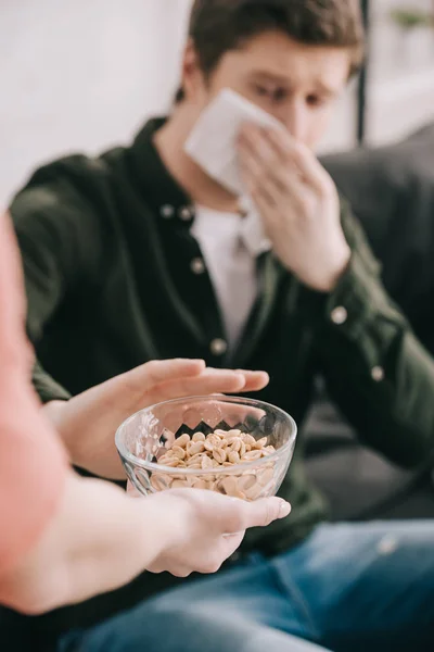Cropped view of woman holding glass bowl with nuts near man with tissue — Stock Photo