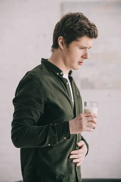 Hombre guapo sosteniendo un vaso de leche mientras tiene intolerancia a la lactosa - foto de stock