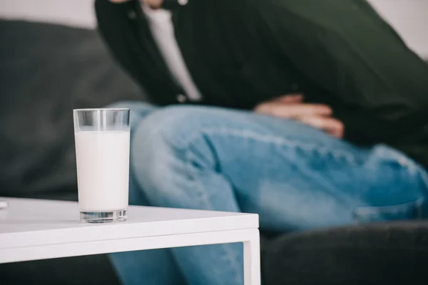 Selective focus of glass of milk on coffee table near man holding stomach — Stock Photo