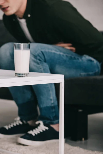 Обрезанный вид человека, держащего желудок и сидящего возле кофейного столика со стаканом молока — стоковое фото