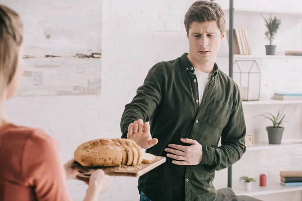 Обрезанный вид женщины, держащей разделочную доску с нарезанным хлебом рядом с красивым мужчиной с аллергией на глютен — стоковое фото