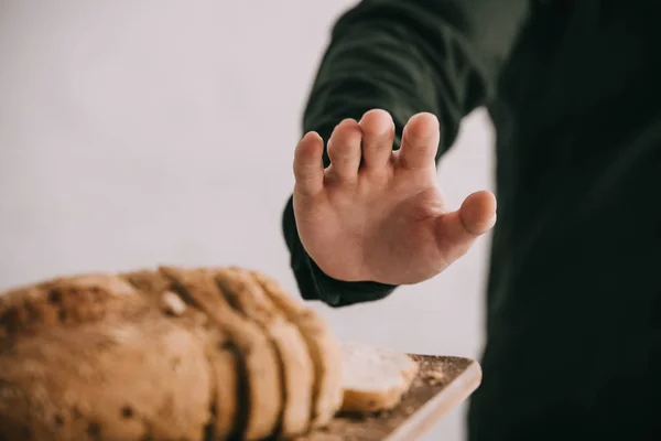 Обрезанный вид человека, жестикулирующего рядом с разделочной доской с нарезанным хлебом, изолированным на сером — стоковое фото