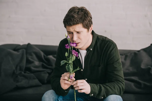 Hombre guapo oliendo flor mientras está sentado en casa - foto de stock