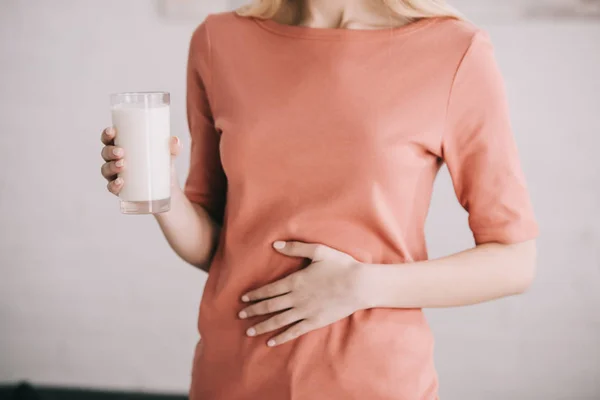Abgeschnittene Ansicht einer Frau, die ein Glas Milch hält, während sie Bauchschmerzen hat — Stockfoto