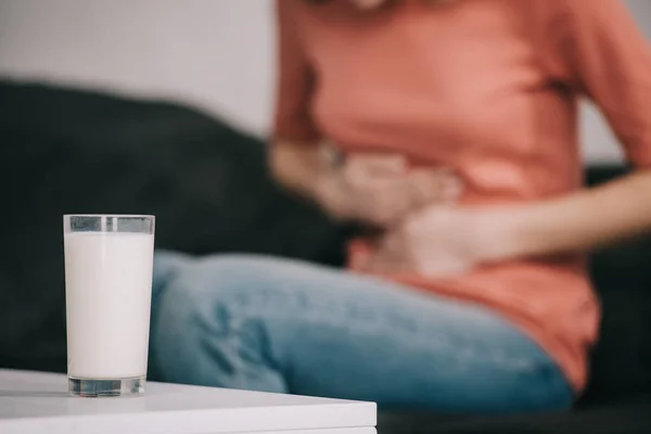 Vista recortada de la mujer con intolerancia a la lactosa que sostiene el estómago cerca del vaso de leche - foto de stock