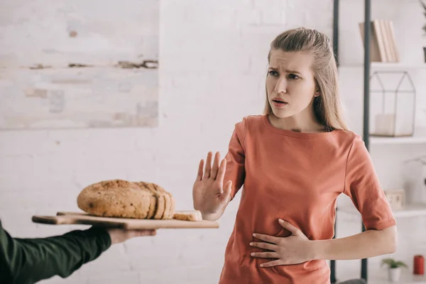 Recortado vista de hombre sosteniendo tabla de cortar con pan cerca molesto mujer rubia con alergia al gluten - foto de stock