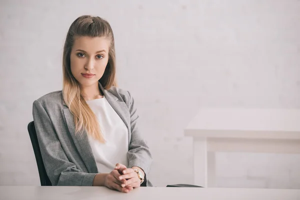 Jolie femme blonde assise avec les mains serrées et regardant la caméra — Photo de stock