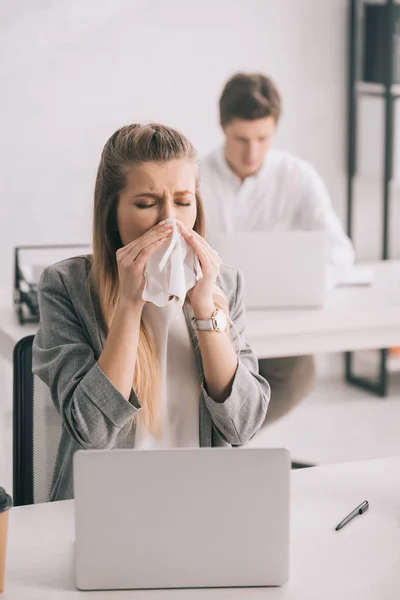 Businesswoman sneezing in tissue near coworker in office — Stock Photo