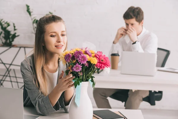 Foyer sélectif de femme gaie regardant des fleurs près de collègue allergique au pollen — Photo de stock