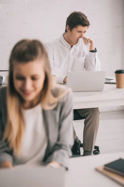 Messa a fuoco selettiva dell'uomo che tiene il tessuto durante l'utilizzo del computer portatile vicino alla donna d'affari in ufficio — Foto stock