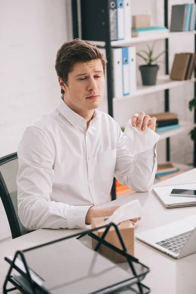 Sad businessman holding tissue while sitting near laptop in office — Stock Photo