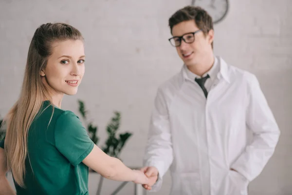Selective focus of cheerful blonde patient shaking hands with happy doctor in white coat — Stock Photo