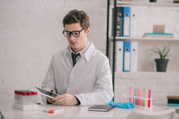 Handsome doctor in glasses and white coat looking at digital tablet — Stock Photo