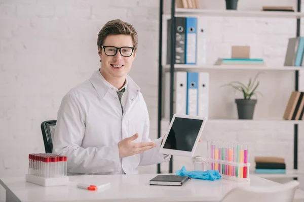 Doctor feliz en gafas y capa blanca mostrando tableta digital con pantalla en blanco - foto de stock