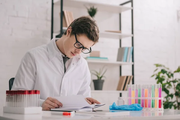 Schöner Arzt mit Brille und weißem Mantel liest Buch — Stockfoto