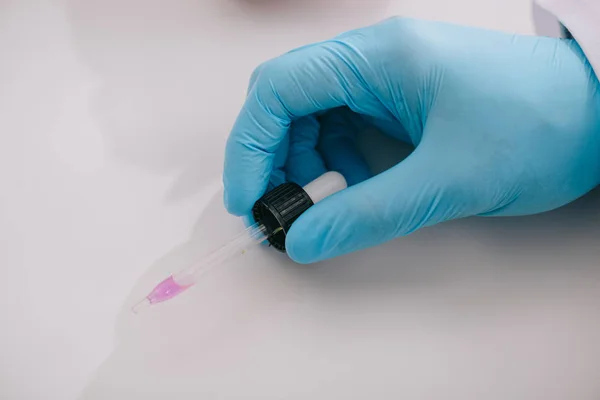 Cropped view of doctor in latex glove holding pipette with liquid — Stock Photo