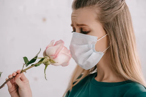 Femme blonde allergique au pollen portant un masque médical et sentant la rose — Photo de stock