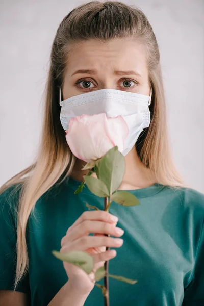 Selective focus of blonde woman in medical mask holding rose in hand — Stock Photo