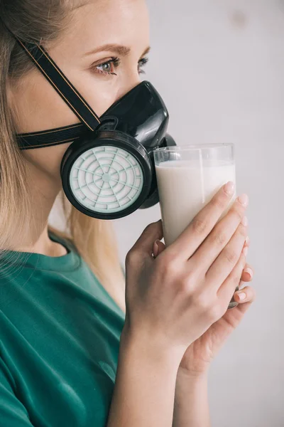 Mujer rubia en máscara respiratoria oliendo leche mientras sostiene el vidrio - foto de stock