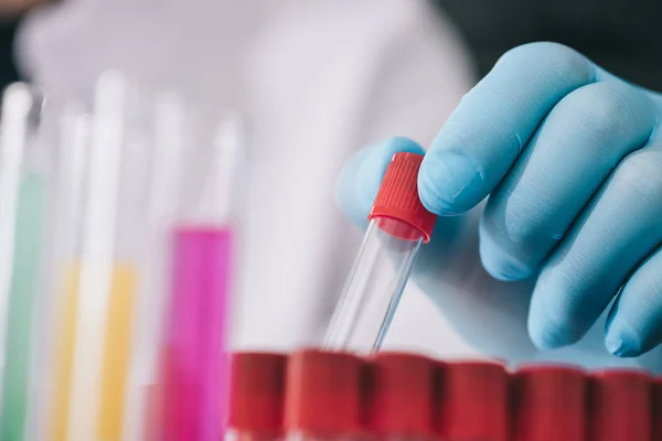 Vista recortada del médico en guante de látex azul sosteniendo tubo de ensayo de vidrio en laboratorio - foto de stock