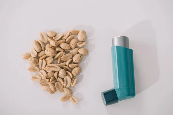 Vista superior de sabrosos cacahuetes nutritivos cerca del inhalador azul sobre gris - foto de stock