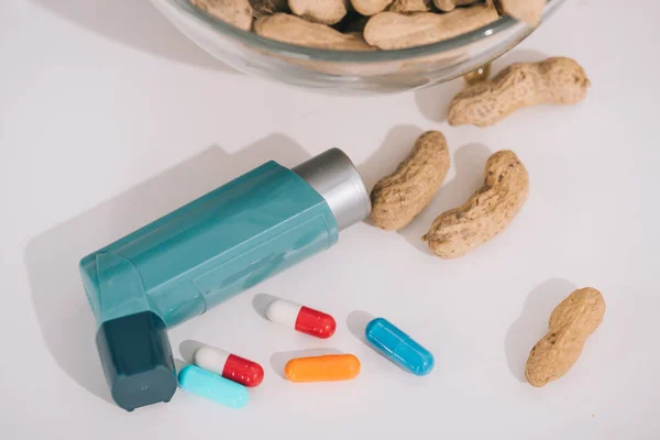 Amendoins saborosos perto do inalador azul e pílulas em cinza — Fotografia de Stock