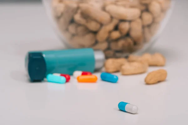 Foyer sélectif de pilules près de cacahuètes savoureuses et inhalateur bleu sur gris — Photo de stock