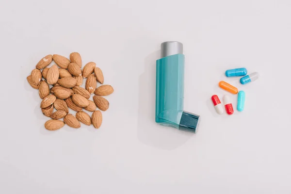 Top view of tasty almonds near pills and blue inhaler on grey — Stock Photo