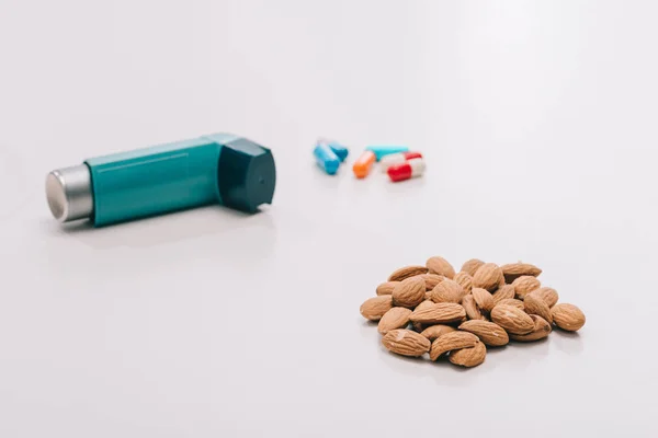 Foyer sélectif d'amandes savoureuses près des pilules et inhalateur bleu sur gris — Photo de stock