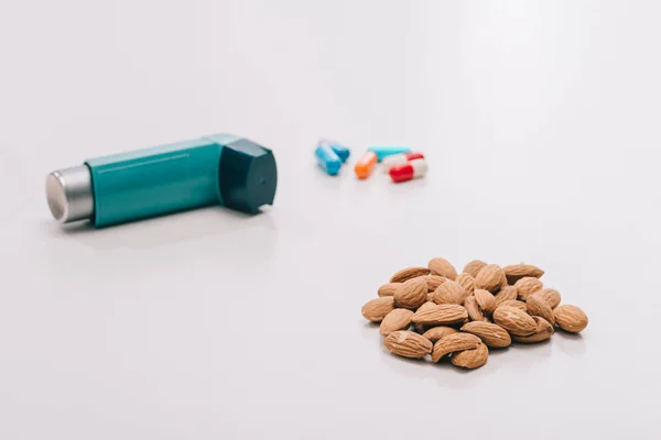Selective focus of tasty almonds near pills and blue inhaler on grey — Stock Photo
