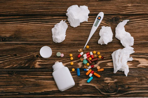 Vue de dessus des tissus blancs près du thermomètre, de la bouteille et des pilules sur la surface en bois — Photo de stock