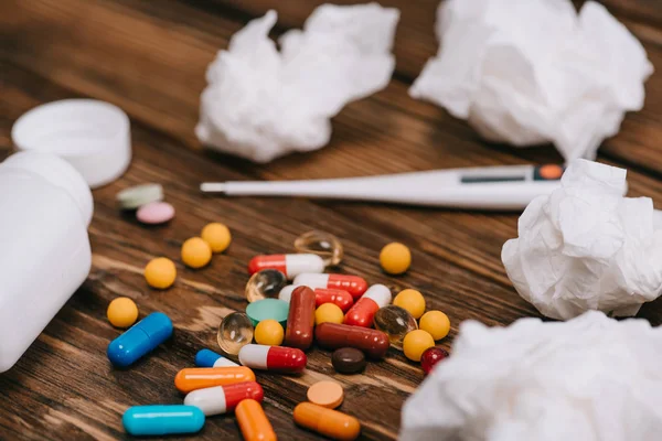 Selective focus of pills near thermometer and white tissues on wooden surface — Stock Photo