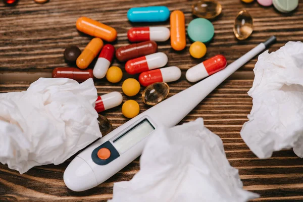 Close up of  of pills near thermometer and white tissues on wooden surface — Stock Photo