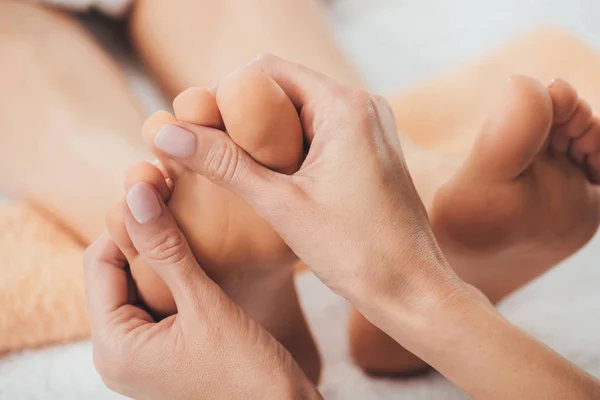 Vista ritagliata del massaggiatore che fa massaggio ai piedi alla donna adulta nella spa — Foto stock