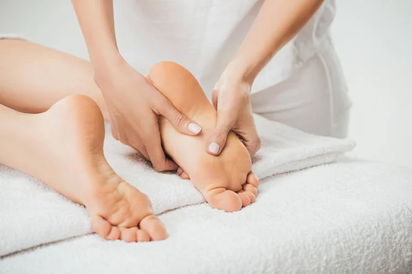 Vista parcial de masajista haciendo masaje de pies a mujer adulta en spa - foto de stock