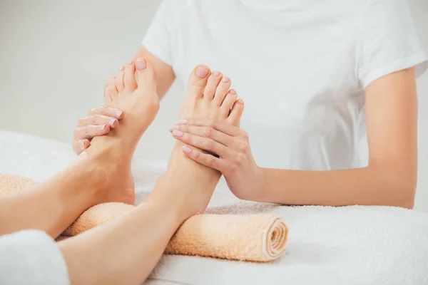 Vista parcial de masajista haciendo masaje de pies a mujer adulta en spa - foto de stock