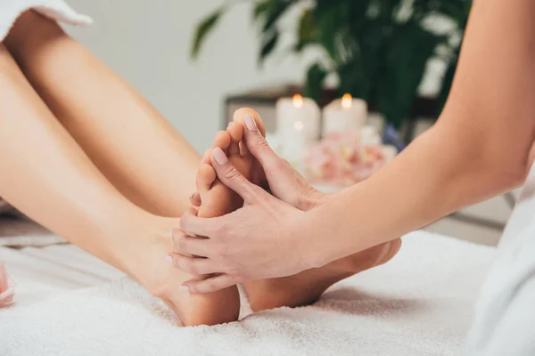 Vista parcial de masajista haciendo masaje de pies a mujer adulta en spa - foto de stock