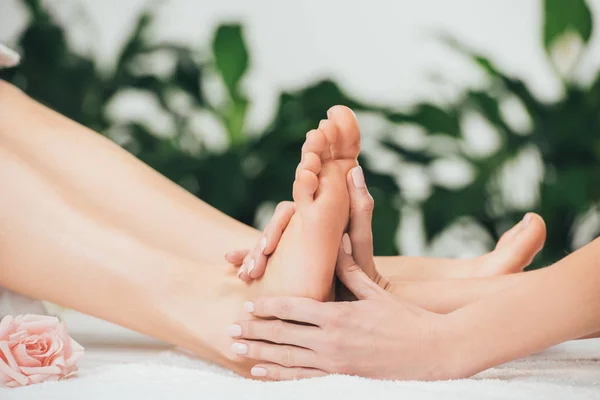 Vista parcial de masajista haciendo masaje de pies a mujer adulta en spa - foto de stock