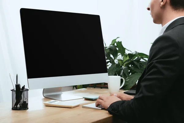 Cropped view of man using computer with blank screen in office — Stock Photo