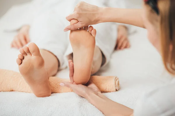 Vista parziale del massaggiatore che fa massaggio ai piedi alla donna adulta nella spa — Foto stock