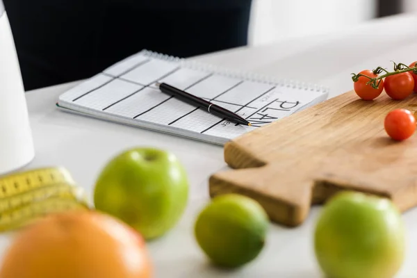 Selective focus of wooden cutting board with cherry tomatoes near notebook with plan lettering — Stock Photo