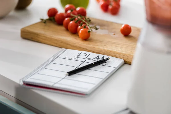 Selective focus of notebook with plan lettering near wooden cutting board with cherry tomatoes — Stock Photo