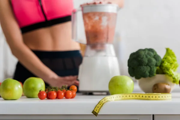 Selektiver Fokus von Äpfeln und Gemüse in der Nähe von Maßband in der Nähe einer Frau, die Smoothie zubereitet — Stockfoto