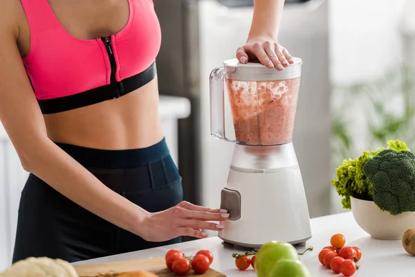 Cropped view of sportswoman preparing smoothie in blender — Stock Photo
