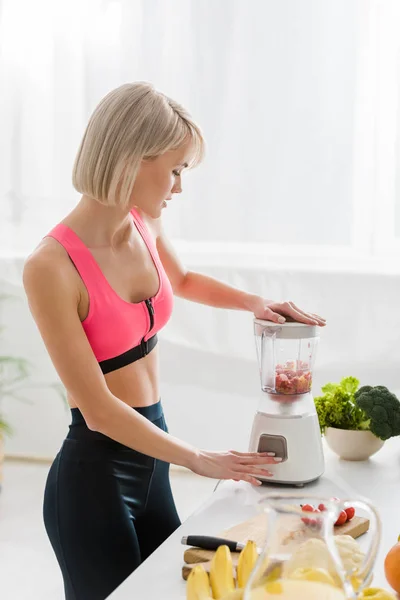 Hermosa deportista rubia mezclando comida en licuadora - foto de stock